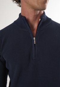Marineblauwe trui met rits en geribbeld textuur; heeft een kwartrits en hoge kraag voor een snug fit. Minimalistisch ontwerp.