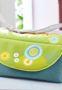 Green and blue handbag with circular patterns and floral accents, made of fabric with a textured finish, featuring a silver strap.