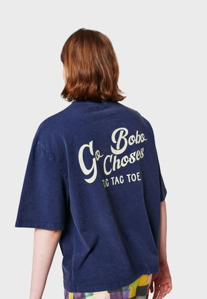T-shirt oversize blu navy in morbido cotone, con grande scritta bianca stampata sul retro che dice "Go Bobo Choses TIC TAC TOE."