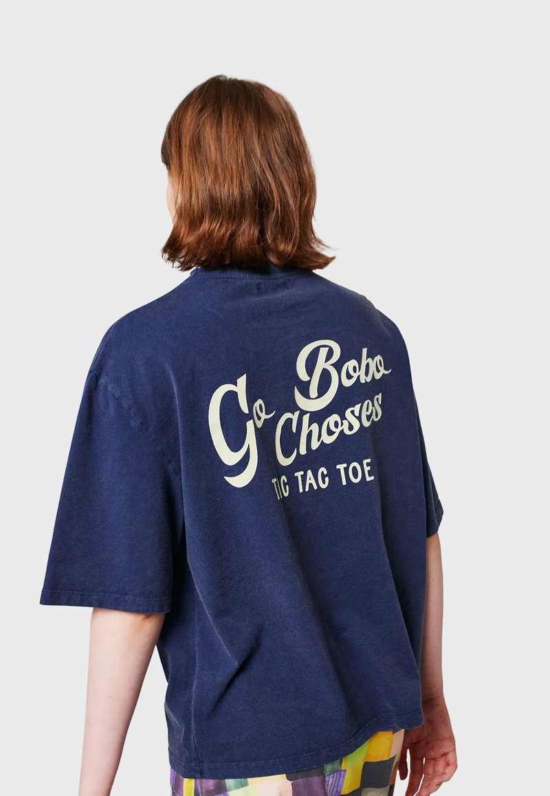 T-shirt oversize blu navy in morbido cotone, con grande scritta bianca stampata sul retro che dice "Go Bobo Choses TIC TAC TOE."
