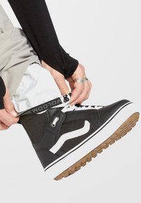 Zapatillas de deporte de caña alta negras con acentos blancos, parte superior de lona texturizada, diseño con cordones y suela de goma de color tostado.