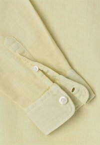 Cavaletto di camicia in lino giallo chiaro con un bottone bianco e un'asola, caratterizzato da una sottile texture e un design pulito e classico.