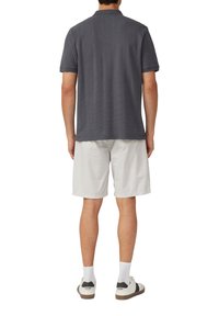 Szara koszulka polo z krótkim rękawem, teksturowany materiał i płaski kołnierz. Połączona z białymi szortami w wzory i casualowymi sneakersami.