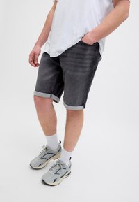 Şorturi din denim de culoare gri închis, cu tivuri rulate, stilizate cu un tricou alb și adidași gri, având un design ușor și casual.