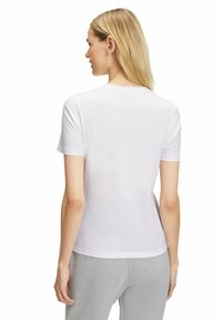 Witte katoenen t-shirt met korte mouwen, ronde hals en een gladde textuur, gedragen met lichtgrijze broek, waarbij de achterzijde zichtbaar is.