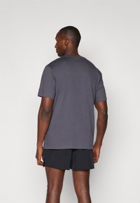 Herren T-Shirt mit kurzen Ärmeln in Dunkelgrau, hergestellt aus weichem Stoff, mit rundem Ausschnitt und lockerer Passform, kombiniert mit schwarzen Shorts.