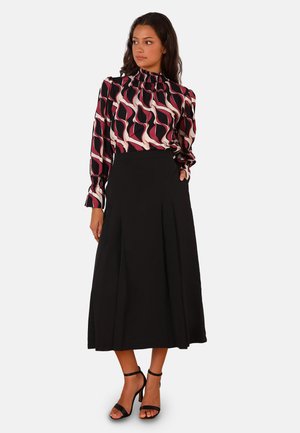 Gonna nera lunga abbinata a una blusa stampata con motivi ondulati rosa e neri. La blusa presenta un collo smock e maniche a sbuffo.