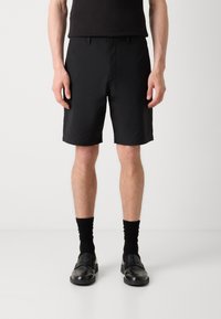 Sorte shorts med rett snitt, laget av lett materiale, med beltehemper og sidelommer. Båret med sorte sokker og loafers.