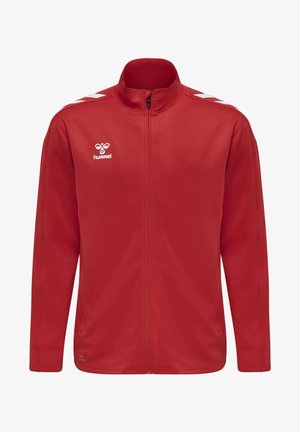 Czerwona kurtka sportowa z pełnym zamkiem błyskawicznym z przodu, białe logo hummel na lewej piersi oraz białe pasy w kształcie jodełki na ramionach.