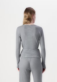 Pruhovaná dlhá rukávová blúzka v šedej a čiernej farbe s priliehavým strihom, okrúhlym výstrihom a detailom viazania v oblasti pásu na zadnej strane.