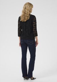 Top nero con maniche in pizzo, abbinato a jeans a zampa d'elefante blu scuro. Vestibilità slim con cuciture dettagliate sui jeans e scarpe col tacco nere.