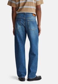 Niebieskie dżinsy o luźnym kroju, z skórzaną naszywką z tyłu i dwiema tylnymi kieszeniami; delikatne wyblaknięcie wzdłuż nogawek.