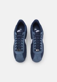 Navy Nike Sneakers aus einer Mischung aus Wildleder und Textilmaterialien, klassisches Low-Top-Design, Schnürverschluss und weißem Swoosh-Logo-Akzent.