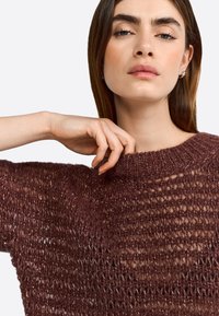 Strickpullover in tiefem Burgunderrot, mit einem offenen Webmuster, weitem Halsausschnitt und kurzen Ärmeln, mit einer weichen, strukturierten Oberfläche.
