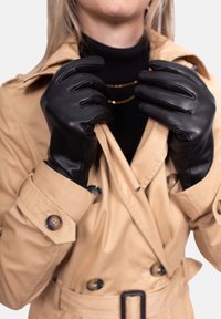 Schwarze Lederhandschuhe, getragen von einer Person in einem beigen Trenchcoat. Die Handschuhe haben eine glatte Textur mit einer taillierten Form und dezenten Nähte.