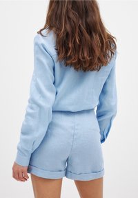 Blouse en lin bleu clair à manches longues avec short assorti à ourlet roulé ; texture lisse et design simple sans motifs ni embellissements.