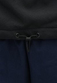 Svart og marineblått stoff sammenkoblet med en svart snor med plastisk lås, sydd søm langs den øverste kanten.