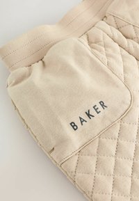 Bež puitud kangas, millel on elastne vöökoht. Omab küljetaskut, millel on tume kiri "BAKER".
