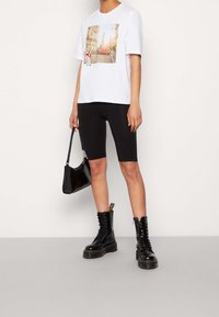 Vit t-shirt med en fram- grafik som visar en gatubild och en röd bil, kombinerad med svarta cykelshorts och svarta snörkängor.