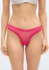 Γυναίκα που φορά απαλά ροζ διαφανή δαντελένια εσώρουχα με μικρά μοτίβα καρδιάς και λευκό σουτιέν, εμφανιζόμενη από τη μέση έως το πάνω μέρος των μηρών.