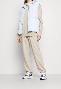 Light blue puffer vest over a beige hoodie and sweatpants. White sneakers with purple and black accents. Smooth, padded texture throughout.