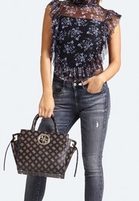 Haut noir à motif floral avec volants transparents, associé à un jean gris déchiré. Sac cabas noir à main avec logo et design structuré.