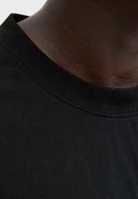 Sort bomulds T-shirt med nærbillede af den runde ribbede hals og glatte tekstur, der viser detaljerne i stoffet og syningerne.