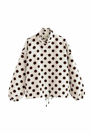 Blusa blanca de manga larga con lunares negros, cuello alto, puños elásticos y cordón en el bajo.