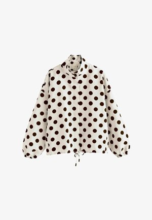 Blusa blanca de manga larga con lunares negros, cuello alto, puños elásticos y cordón en el bajo.