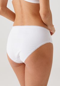 Witte katoenen slips met een gladde textuur, voorzien van een geschulpte kantafwerking langs de tailleband en de beenopeningen. Standaard slipvorm.