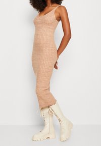 Robe côtelée, de longueur mi-mollet, beige avec des fines bretelles, associée à des bottes blanches à lacets montantes avec une semelle épaisse.