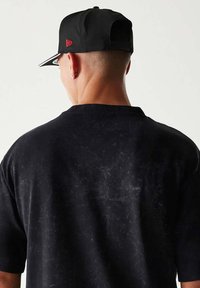 Czarna koszulka krótki rękaw z teksturowaną powierzchnią, noszona z czapką w kolorze czarnym z czerwonym logo z tyłu. Prosty, swobodny design.