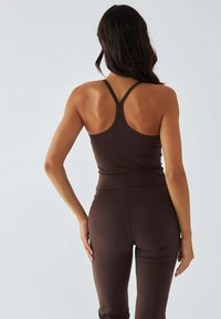 Brązowy sportowy top na cienkich ramiączkach z tłoczonym tyłem typu racerback, zestawiony z legginsami z wysokim stanem. Gładka faktura, dopasowany krój, minimalne dodatki.