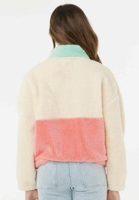 Chaqueta de forro polar en colores crema, menta y coral; diseño oversize con un acabado suave y texturizado, que presenta secciones en bloque de color.