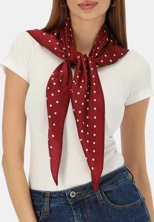 Kobieta ubrana w biały krótki rękaw, zawiązaną bordową chustę w białe kropki oraz niebieskie dżinsy.