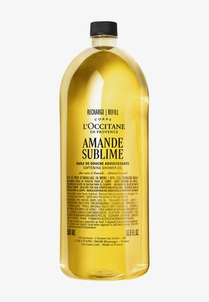 Recharge d’huile de douche adoucissante à l’amande L’Occitane, dans une grande bouteille transparente remplie d’huile dorée et munie d’un bouchon noir.