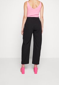 Pantalon noir à jambes larges avec poches latérales, associé à un débardeur côtelé rose clair et des sandales à talons hauts rose vif.