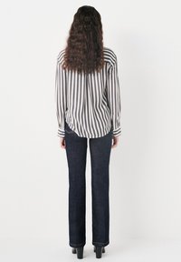 Chemise rayée blanche et grise, avec une coupe ample et un ourlet arrondi, associée à un jean en denim bleu foncé. Les deux vêtements ont des manches longues.