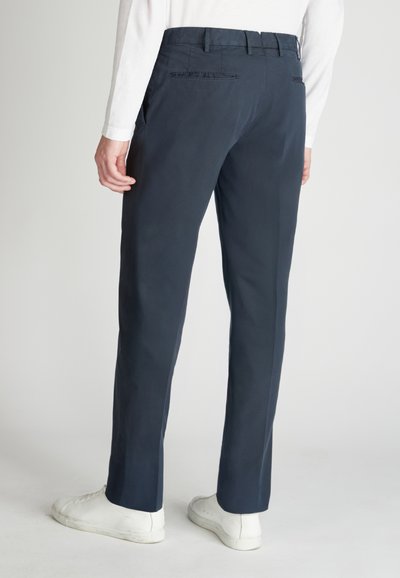 Pantaloni navy con taglio dritto, dotati di una cintura con passanti e due tasche posteriori. Indossati con sneakers bianche.