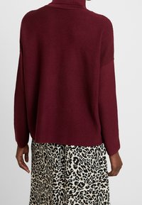 Maglione a coste bordeaux con collo alto e spalle basse, abbinato a una gonna a stampa leopardata. Presenta una vestibilità comoda.