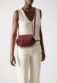 Burgundy leather crossbody bag with a flap closure, gold hardware, and textured finish. Features a shoulder strap and side pocket.