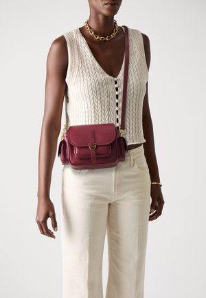 Burgundy leather crossbody bag with a flap closure, gold hardware, and textured finish. Features a shoulder strap and side pocket.