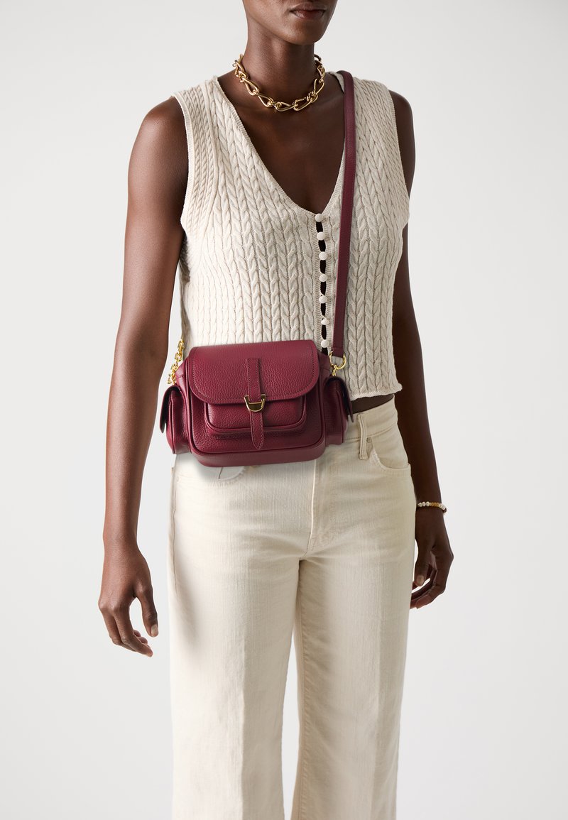 Burgundy leather crossbody bag with a flap closure, gold hardware, and textured finish. Features a shoulder strap and side pocket.