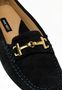 Sorte flade sko i ruskind med guldfarvet hardware, kontrastsyninger og rund tådesign. Indvendig beklædt med beige materiale, mærket "Nine West."