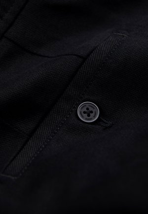 Tissu noir texturé avec un motif de tissage diagonal, comprenant un bouton noir rond avec des détails en relief et une poche slim.