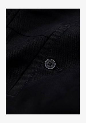 Black textured fabric with a diagonal weave pattern, featuring a round black button with embossed detailing and a slim pocket.