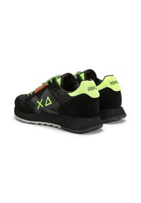 Zapatillas deportivas negras con parte superior de ante y malla, acentos en verde neón, cordones de cuerda y suela de goma gruesa. Logo distintivo en el lateral.