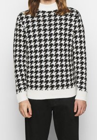 Jersey de punto en patrón de ajedrez blanco y negro con un cuello redondo acanalado y puños, que presenta un acabado texturizado.