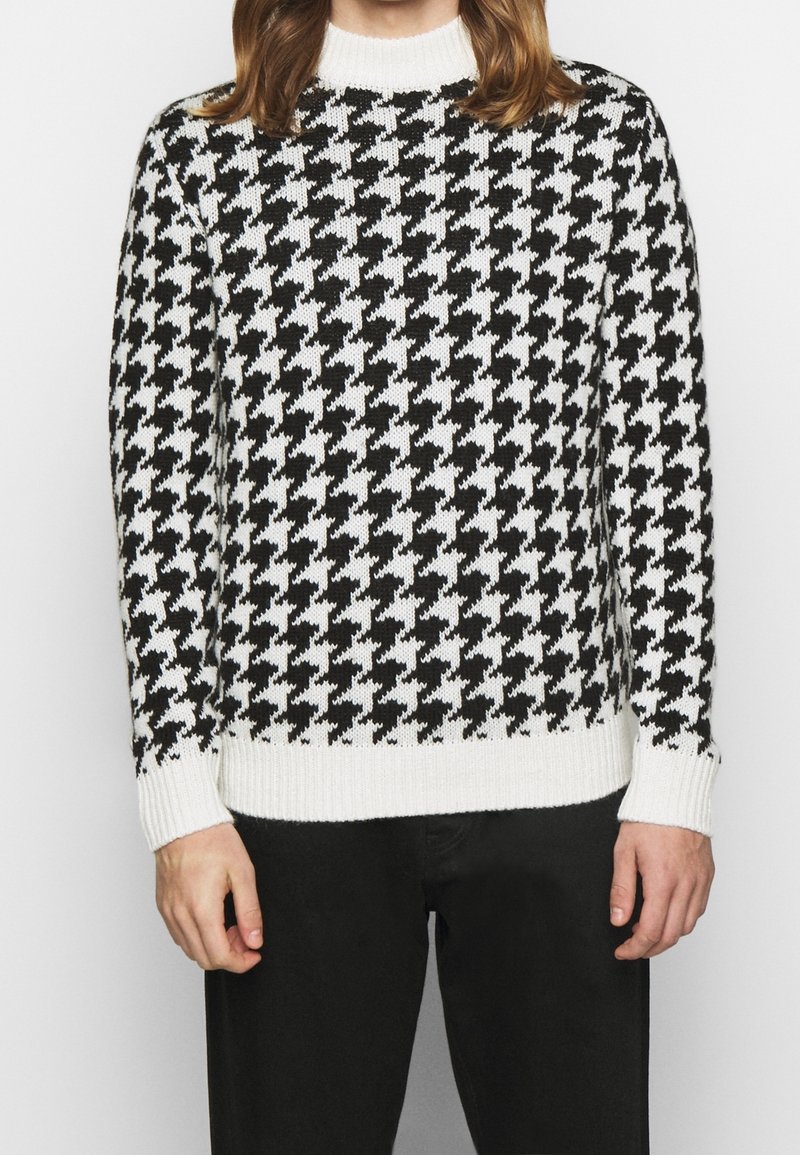 Jersey de punto en patrón de ajedrez blanco y negro con un cuello redondo acanalado y puños, que presenta un acabado texturizado.