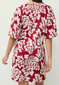 Robe courte à manches courtes fleurie rouge avec des motifs de feuilles blanches, un col incurvé et une coupe décontractée, fabriquée en tissu léger.